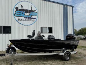 Black fishing boat on trailer beside building.